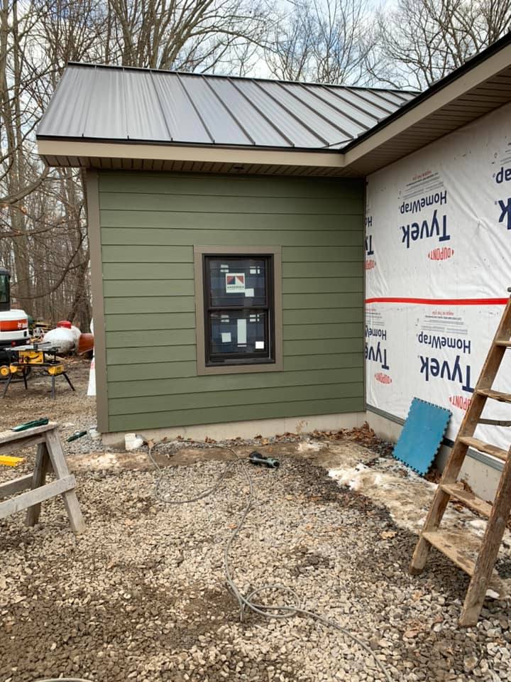New home exterior under construction with metal roof, partial siding installation, and Tyvek house wrap on remaining sections.