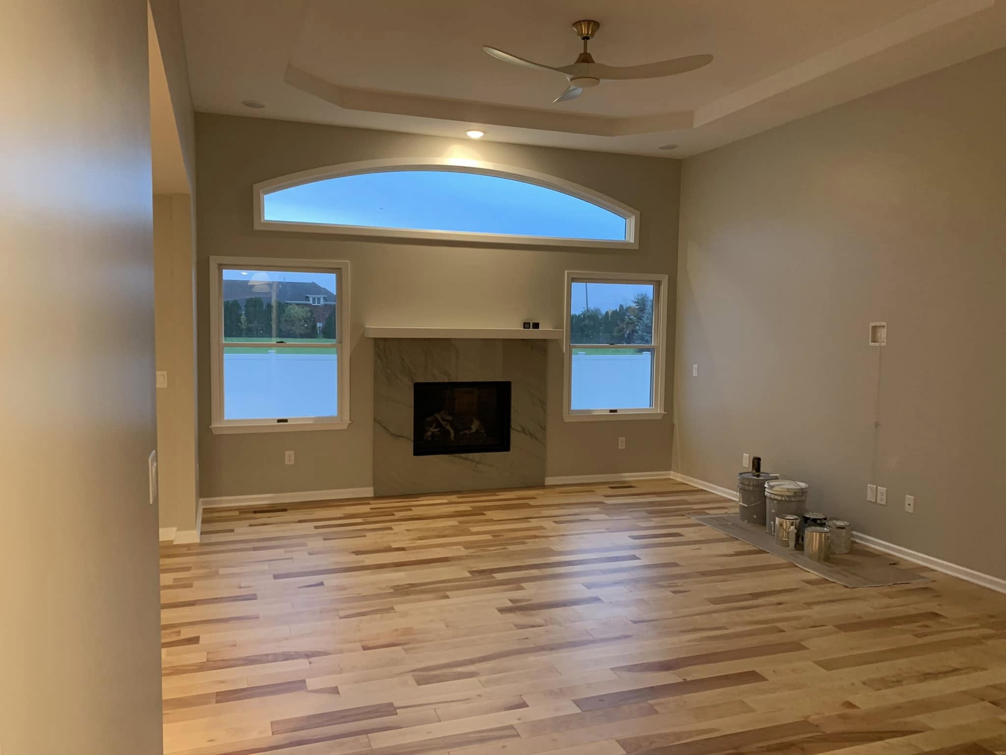 Finished living room interior featuring a fireplace with marble surround, large windows, recessed ceiling, and newly installed flooring.