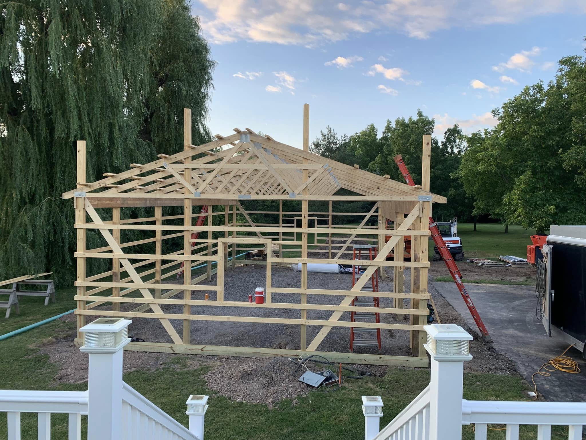 Post‑frame building under construction with roof trusses installed and ladders positioned around the structure.