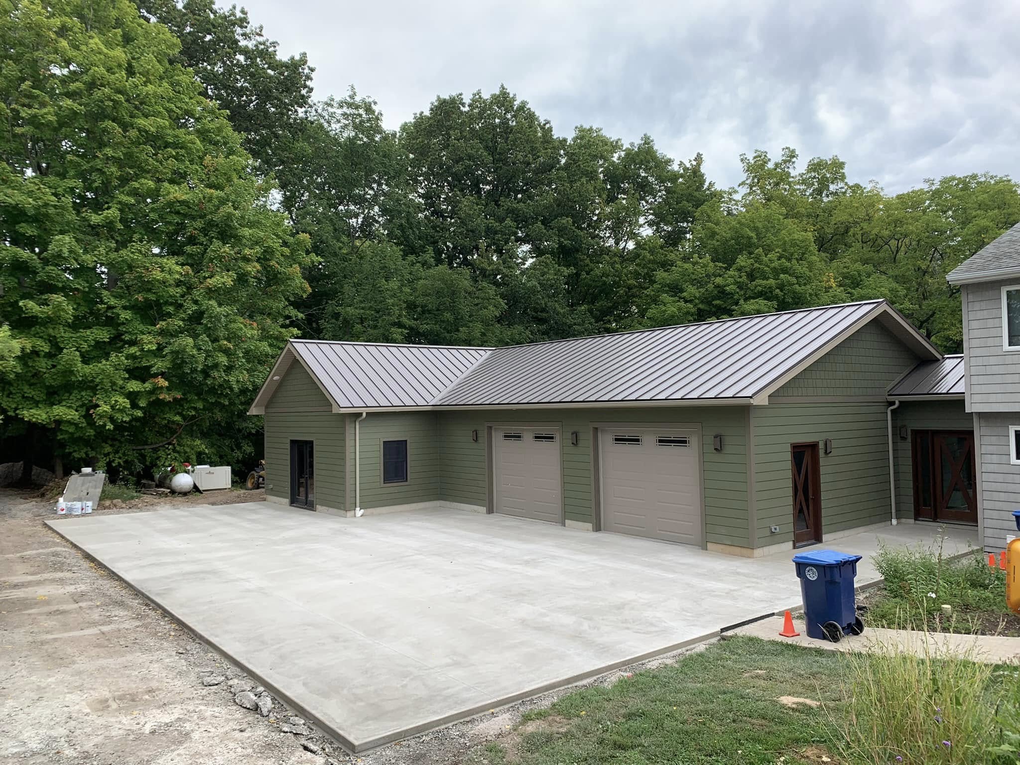 Newly constructed three‑door garage with metal roof and poured concrete driveway by Fournier Construction &amp; Excavation.