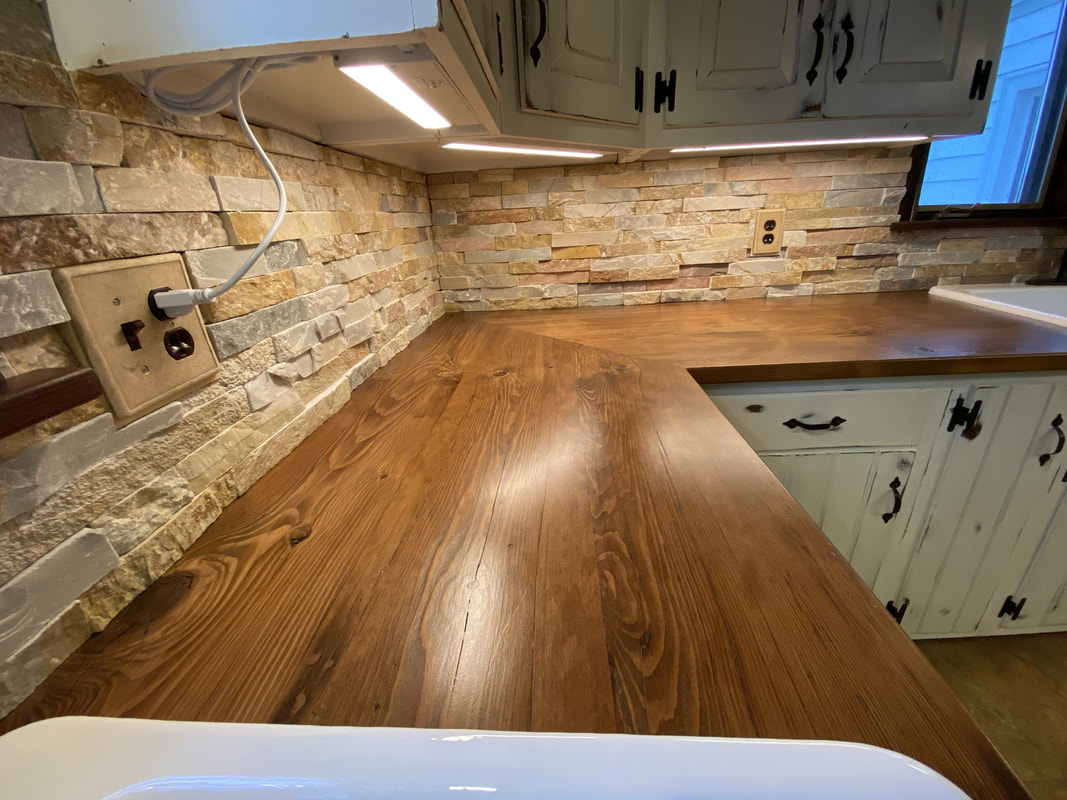 Finished kitchen corner featuring reclaimed barn‑wood countertop and stacked‑stone backsplash under warm under‑cabinet lighting.