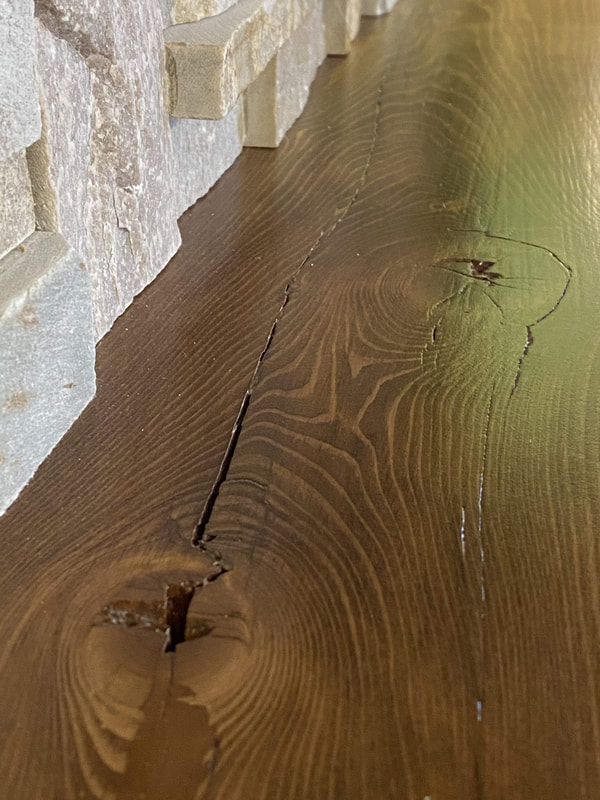 Reclaimed barn‑wood countertop with natural knots and grain beside stacked‑stone backsplash.