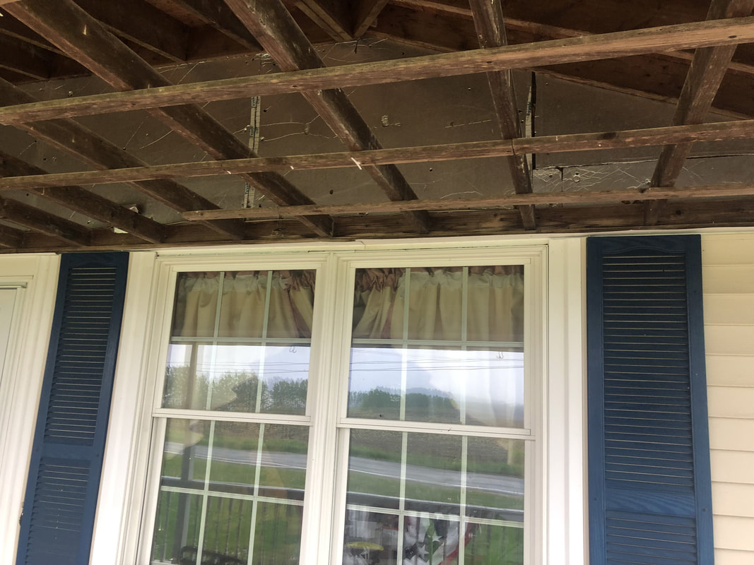 Porch ceiling with old material removed, exposing wooden beams and rafters during ceiling renovation.