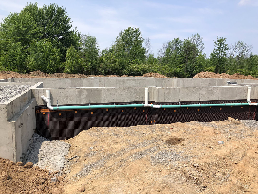 Foundation wall with waterproofing membrane and perimeter drainage pipes installed during excavation.