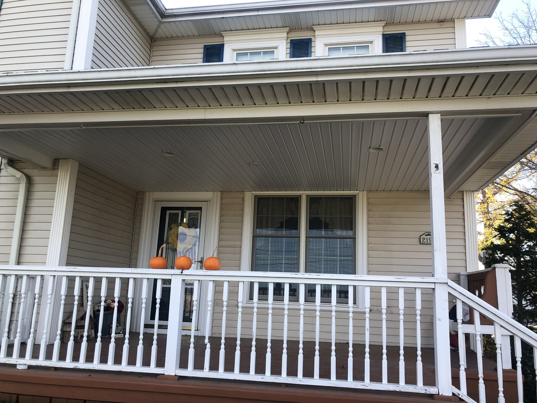 Front porch with new white vinyl ceiling panels installed, pumpkins on railing, and updated exterior appearance.