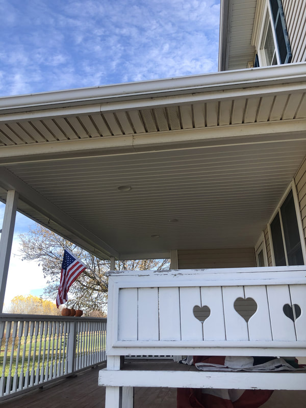 Covered porch with white railing and seasonal decorations, showing completed vinyl ceiling installation.
